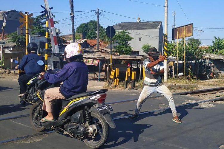 Diryan (55) alias Kopral, penjaga perlintasan sebidang rel kereta api Proyek, Bekasi Timur yang kondang dengan gerakan silatnya tengah melancarkan aksinya, Selasa (23/7/2019).