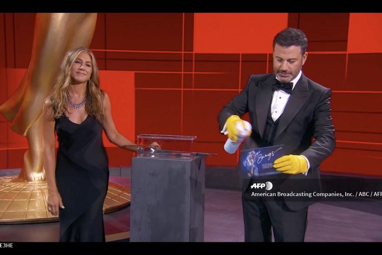 Pembawa acara Jimmy Kimmel dan aktris Jennifer Aniston hendak membacakan pemenang salah satu pemenang Emmy Awards 2020, Minggu (20/9/2020). Jimmy Kimmel menyemprotkan disinfektan pada amplop pemenang.