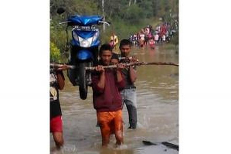 Sejumlah orang sedang menggotong satu unit sepeda motor milik pengendara yang ingin menyeberangi jalan menuju Kampung Tawar Bengi, Kecamatan Jagong Jeget, Kabupaten Aceh Tengah, Aceh, Minggu (25/10/2015).