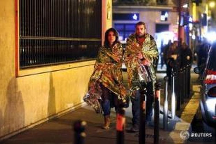 Warga yang lolos dari maut berjalan menghangatkan diri dengan selimut thermal paska rangkaian serangan teroris berdarah yang mengguncang Paris, Jumat (13/11)