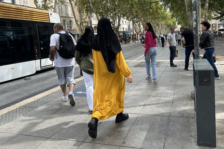 Seorang perempuan mengenakan gaun abaya (kuning) berjalan di jalanan Marseille, Perancis selatan, pada 29 Agustus 2023. Abaya -gaun panjang yang menjuntai dari Timur Tengah akan dilarang untuk siswi sekolah, kata Menteri Pendidikan Perancis, Gabriel Attal kepada wartawan pada 27 Agustus 2023, saat para siswa bersiap untuk kembali ke ruang kelas mereka setelah liburan musim panas. 