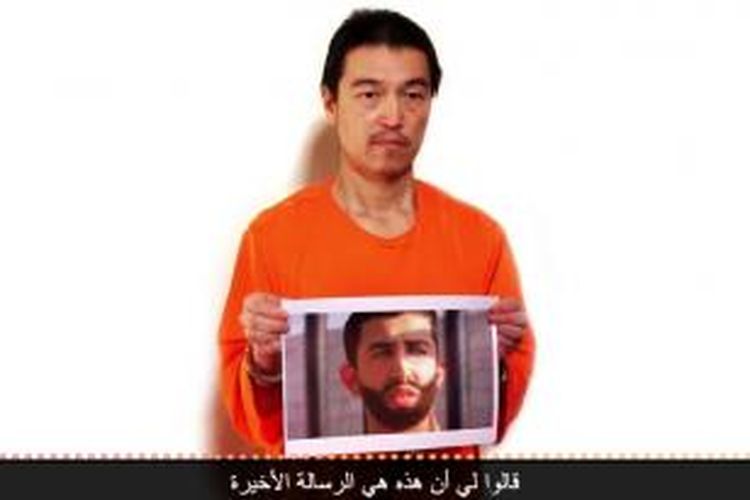 Foto yang diambil dari video yang dirilis Negara Islam Irak dan Suriah (ISIS) menampilkan Kenji Goto, jurnalis Jepang yang kini disandera ISIS, memegang foto seorang pilot AU Jordania. ISIS mengancam akan membunuh keduanya dalam 24 jam jika pemerintah Jordania menolak pertukaran tahanan yang ditawarkan ISIS.