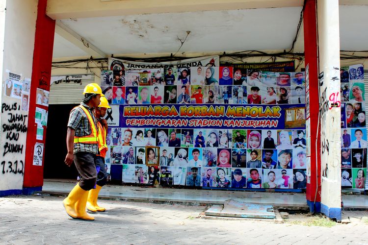 Pekerja proyek renovasi dan revitalisasi pasca Tregedi Kanjuruhan melewati banner penolakan keluarga korban yang berada di gate 13 di Stadion Kanjuruhan Kepanjen, Kabupaten Malang, Selasa (19/9/2023) siang.