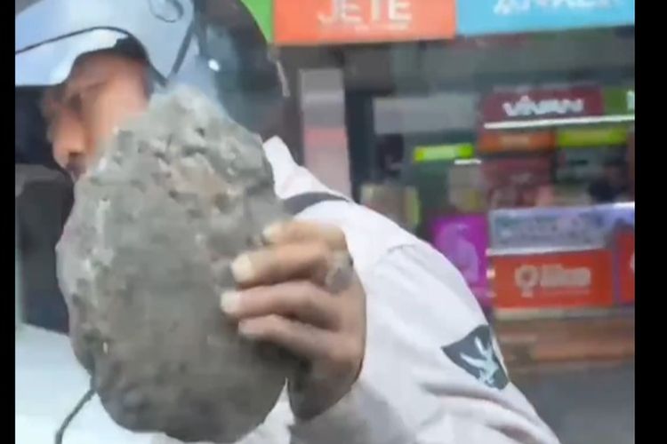 Tangkapan layar dari video viral di media sosial yang menunjukkan seorang pengendara sepeda motor memukul bagian spion mobil memakai batu berukuran cukup besar. 