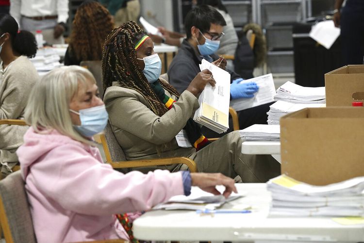 Petugas pemilu check-in, menyortir, dan tanda tangan memverifikasi surat suara yang tidak hadir untuk negara bagian AS. 