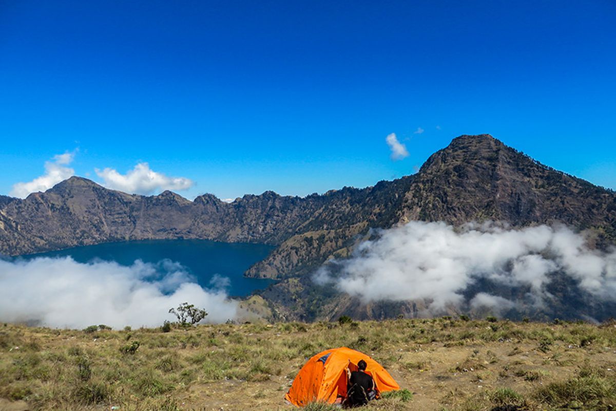 Seorang pendaki dan tendanya dengan latar belakang Segara Anak di Gunung Rinjani.