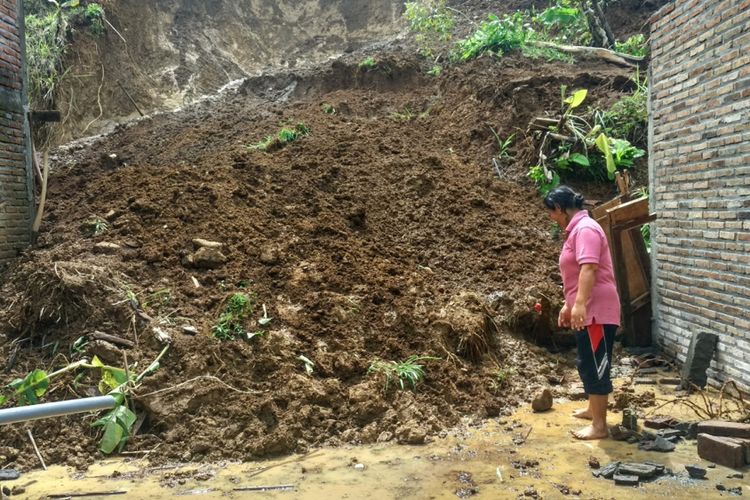 Pemilik rumah (Suratin) diantara material longsor yang menghancurkan dinding bagian belakang rumah (10/12/2018).