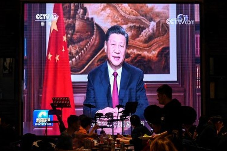 Orang-orang makan malam di sebuah restoran saat layar menayangkan pidato Tahun Baru Presiden China Xi Jinping di Beijing pada 31 Desember 2021. 