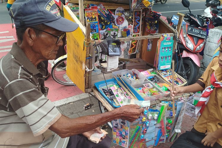 Ahmad melayani anak sekolah yang membeli mainan tradisional tembak bambu yang dijualnya di depan SDN Lateng Banyuwangi, Sabtu (11/1/2025).