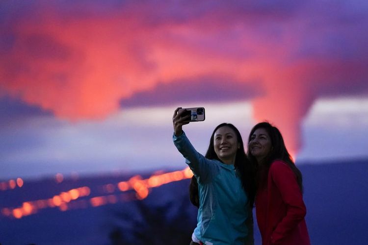 Pengunjung berpose di depan letusan Mauna Loa Hawaii, Rabu (30/11/2022).