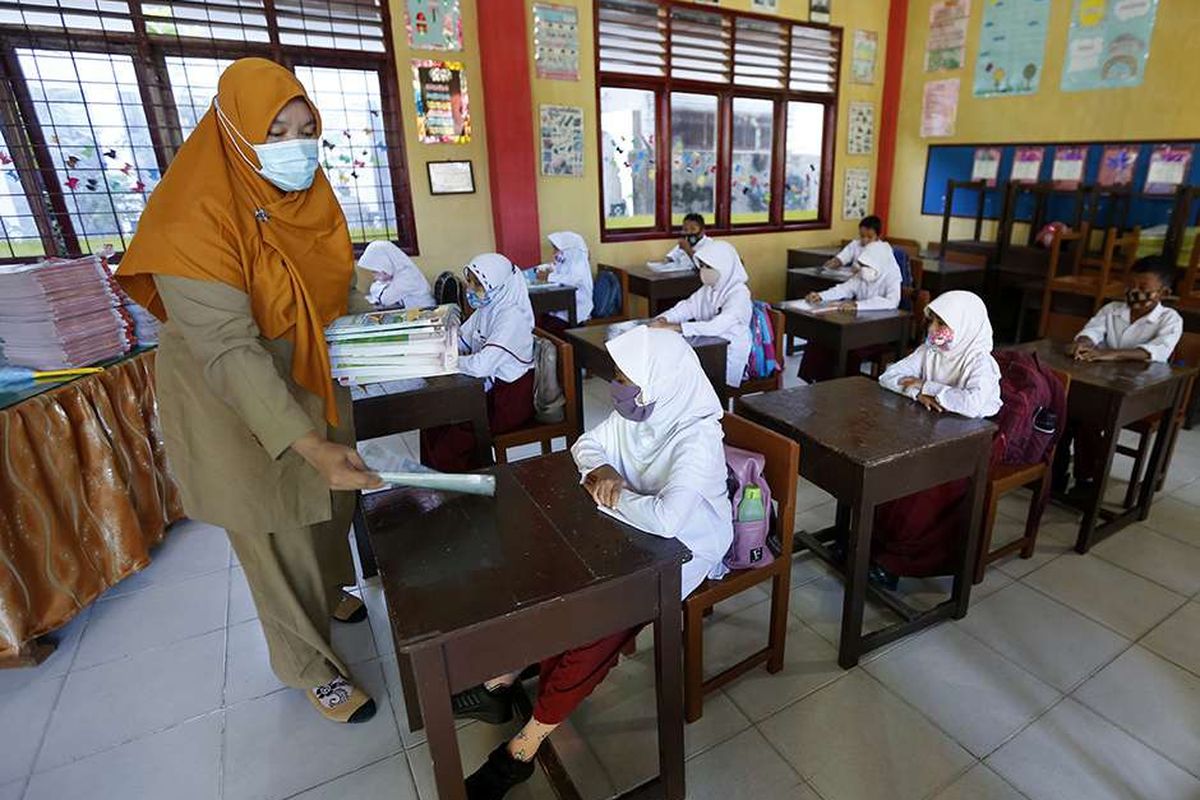 Guru membagikan buku pelajaran kepada pelajar pada hari pertama sekolah tatap muka di SD Negeri 42, Banda Aceh, Aceh, Senin (4/1/2021). Mayoritas lembaga pendidikan tingkat SD, SMP dan SMA di provinsi Aceh mulai melaksanakan pembelajaran tatap muka dengan sistim bergiliran dan menerapkan protokol kesehatan secara ketat untuk mencegah penularan Covid-19.