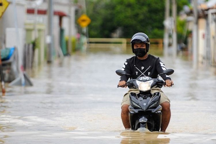Seorang pria mengendarai sepeda motornya melewati banjir