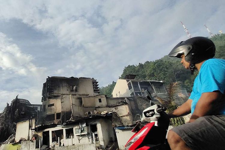 Seorang warga melintasi puing bangunan yang terbakar seusai aksi unjuk rasa di Jayapura, Papua, Jumat (30/8/2019). Sejumlah bangunan dan kendaraan terbakar saat aksi unjuk rasa yang berakhir rusuh di Jayapura, Kamis kemarin, masih terkait memprotes dugaan tindak rasisme kepada mahasiswa Papua di Jawa Timur beberapa waktu lalu.