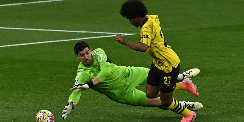 Kiper Real Madrid, Thibuat Courtois, saat menggagalkan tendangan penyerang Borussia Dortmund, Karim Adeyemi, dalam laga final Liga Champions 2023-2024. Duel Borussia Dortmund vs Real Madrid digelar di Stadion Wembley, London, Inggris, Minggu (2/6/2024) dini hari WIB. (Photo by Ben Stansall / AFP)