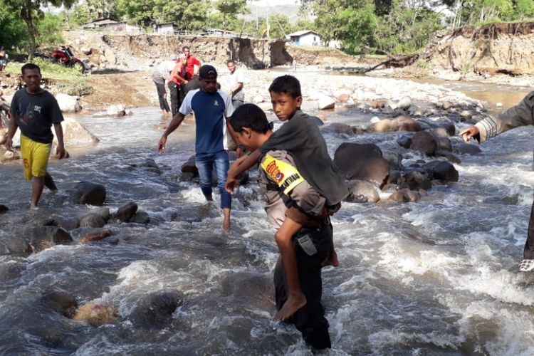 Bripka Safrul Senja Putra membantu warga menyeberangi di Kali Dagemage, Flores, NTT, Jumat (18/1/2019).