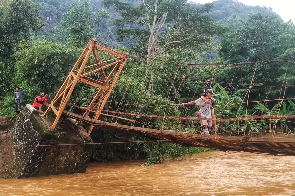 Seorang pria menggendong anaknya menyeberangi di jjembatan gantung nyaris ambruk di Desa Ciemas, Kecamatan Ciemas, Sukabumi, Jawa Barat, Selasa (13/9/2022).
