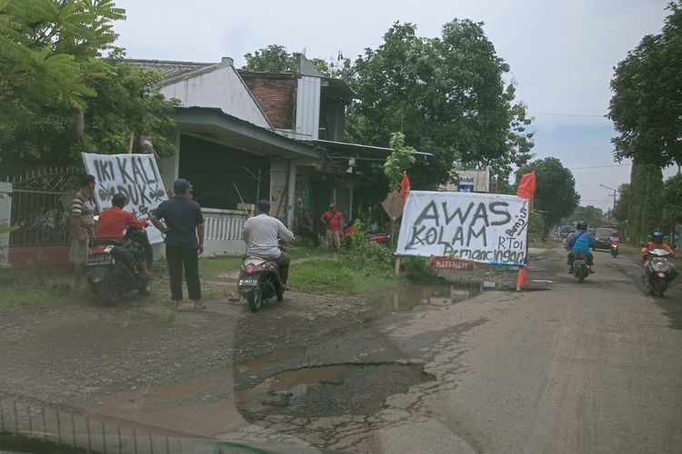Warga Desa Mondo, Kecamatan Mojo, Kabupaten Kediri, Jawa Timur, secara swadaya memasang spanduk di jalan berlubang agar pengguna jalan berhati-hati.
