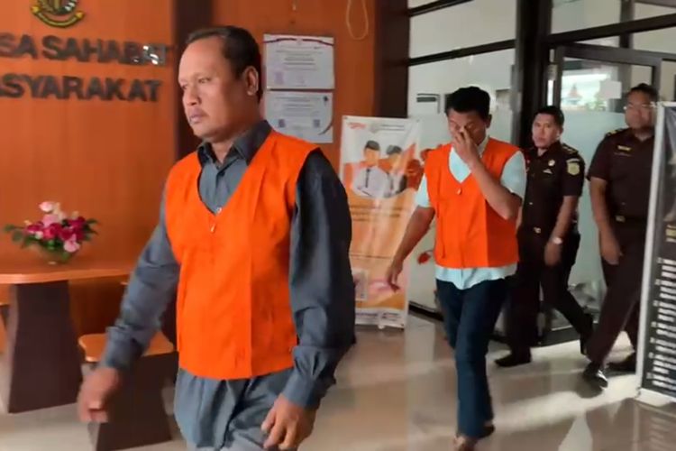 Mantan Kades Cabean-Madiun, Andi Wibowo Kusomo dan mantan sekdesnya, Wahyudi mengenakan rompi oranye digiring ke mobil untuk ditahan di Lapas Kelas I Madiun, Kamis (7/12/2023). Keduanya ditahan dalam kasus dugaan korupsi tukar guling pembebasan tanah proyek ruas tol Madiun tahun 2016-2017.   