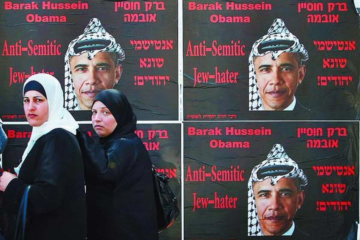 Wanita Palestina berjalan melewati tembok yang ditempeli poster Presiden Amerika Serikat Barack Obama di Jerusalem, Minggu (14/6).