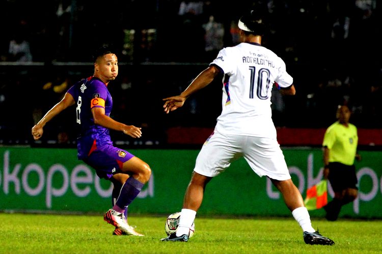 Kapten Persik Kediri Arthur Irawan menjega legenda sepak bola Ronaldinho saat Trofeo Meet The Star melawan RANS Nusantara FC di Stadion Kanjuruhan Kepanjen, Kabupaten Malang, Minggu (26/6/2022) malam. Arthur Irawan saat ini jadi perbincangan akibat video dirinya marah kepada penonton.