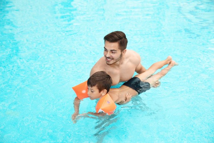 Ilustrasi orangtua mengajarkan anaknya cara berenang.