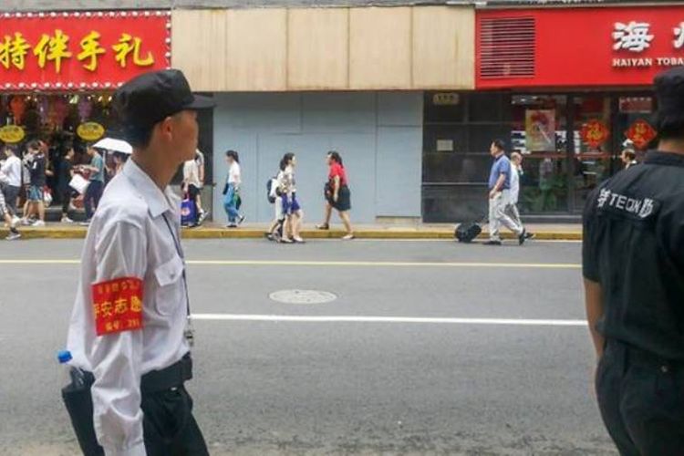 Warga melintas di bawah lokasi jatuhnya papan reklame di tepi jalan Nanjing Timur, di pusat perbelanjaan yang ramai di Shanghai, pada Minggu (12/8/2018) malam.