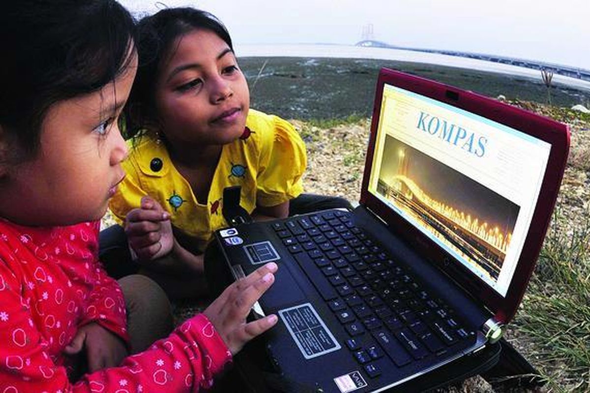 Dua anak melihat halaman Kompas melalui fasilitas e-paper yang diakses dengan koneksi internet menggunakan komputer jinjing di kawasan sekitar Jembatan Suramadu di pantai Desa Sukolilo, Kecamatan Labang, Kabupaten Bangkalan, Madura, Jawa Timur, beberapa waktu lalu.