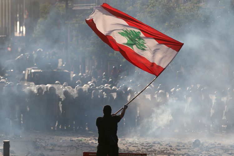 Seorang demonstran mengibarkan bendera Lebanon di depan pasukan polisi, dalam aksi unjuk rasa di Beirut, Lebanon, pada Sabtu (8/8/2020).