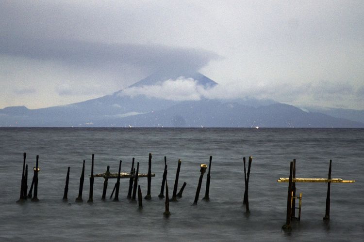 Gunung Agung di Kabupaten Karangasem, Bali, tertutup awan, terlihat dari pinggiran Pantai Ampenan, Mataram, NTB, Selasa (21/11/2017). Letusan yang terjadi pada pukul 17.05 Wita ditandai dengan asap berwarna kelabu dan abu vulkanik tipis yang membumbung dari puncak kawah dengan tekanan sedang hingga tinggi maksimum 700 meter, dan abu letusan bertiup ke arah timur-tenggara.