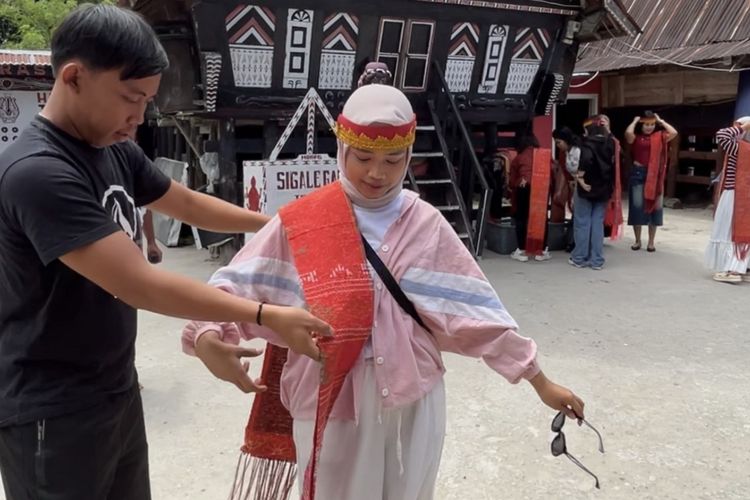 Wisatawan memakai ulos dan sortali sebelum ikut manortor di Sigale-gale, Desa Tomok, Kabupaten Samosir, Sumatera Utara, Jumat (16/5/2025). 