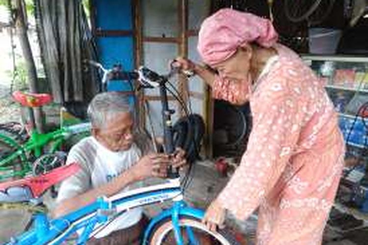 Pasangan Sukadi (kiri) dan Ruminem saat memperbaiki sepeda pancal di bengkel miliknya.