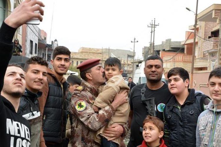 Sejumlah warga kota Mosul berfoto bersama seorang anggota pasukan khusus Irak yang bertempur merebut kota itu dari tangan ISIS.