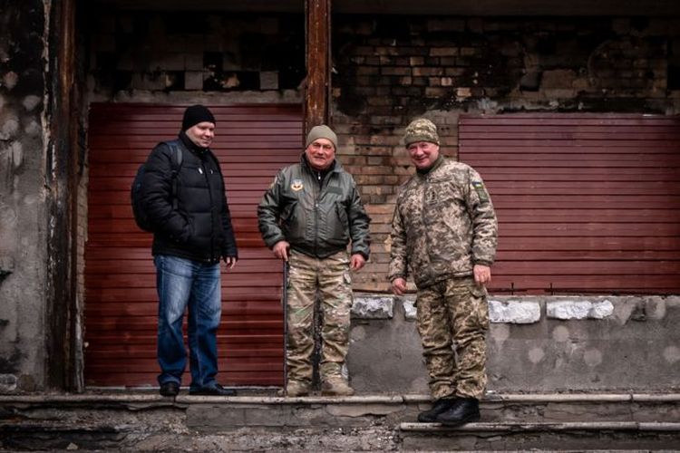 Maksym (kiri), Volodymyr (tengah) dan 'si kolonel (kanan) berdiri di depan kantor yang dibom, yang digunakan oleh relawan lokal.