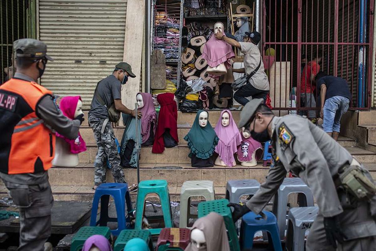 Petugas Satpol PP membantu pedagang mengemas barang dagangnya saat berpatroli di kawasan Pasar Tanah Abang, Jakarta, Sabtu (23/5/2020). Patroli gabungan yang diikuti oleh Satpol PP, Polri, dan TNI tersebut bertujuan untuk menghimbau kepada para pedagang untuk tidak berjualan selama penerapan Pembatasan Sosial Berskala Besar (PSBB) untuk pencegahan penyebaran COVID-19.