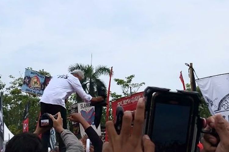 Calon presiden nomor urut 3, Ganjar Pranowo nampak menyerahkan rompi berwarna hitam di tengah-tengah orasi di Alun-alun Wates, Kulon Progo, Daerah Istimewa Yogyakarta (DIY), Minggu (28/1/2024).
