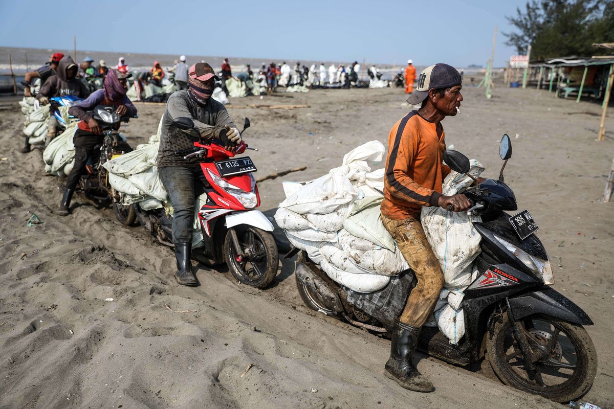 Warga menggunakan motor untuk mengangkut karung yang berisi tumpahan minyak Oil Spill yang tercecer milik Pertamina di Pesisir Pantai Cemarajaya, Karawang, Jawa Barat, Minggu (4/8/2019). Pasir yang tercemar minyak tersebut dikumpulkan dan akan dipindahkan ke pabrik penyimpanan limbah B3 (Bahan Berbahaya dan Beracun) untuk dimusnahkan.