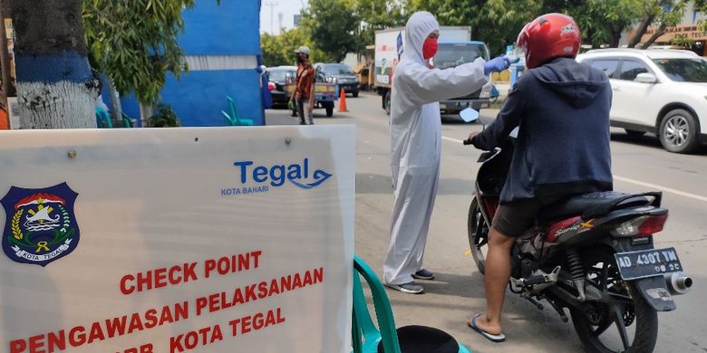 Petugas paramedis memeriksa suhu tubuh menggunakan thermo gun bagi warga yang melintasi posko check point di Jalan Proklamasi, Kota Tegal, Jawa Tengah saat pelaksanaan PSBB, Kamis (7/5/2020)