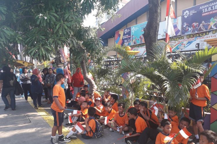 Anak-anak sekolah duduk lesehan di trotoar Jalan Yos Sudarso, Jakarta Utara, menanti kedatangan pawai obor Asian Games 2018, Kamis (16/8/2028)