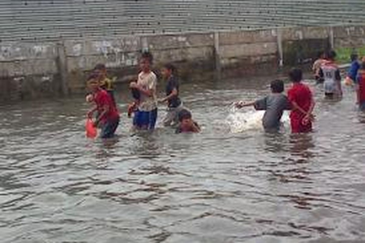 Anak-Anak memanfaatkan banjir di Jalan Masjid At-Taqwa, Kembangan, Jakarta Barat sebagai wanaha berenang gratis, Selasa (10/2/2015).