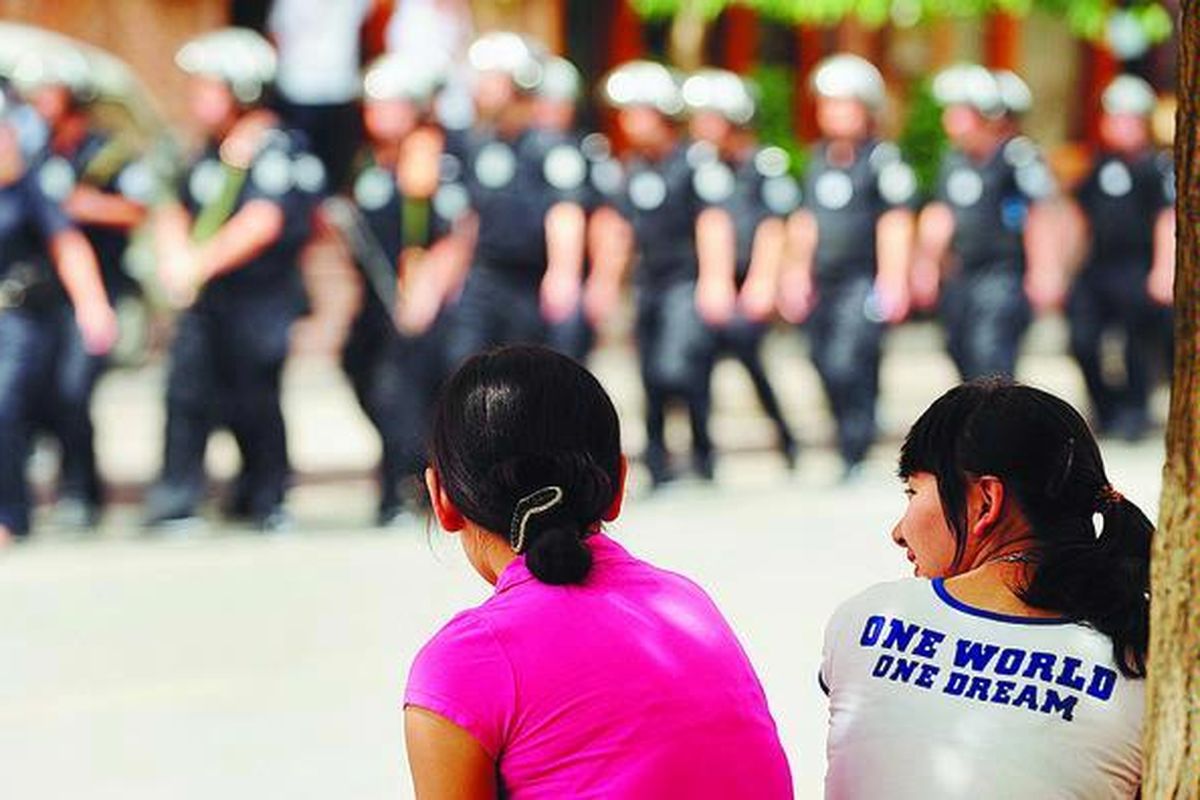 Dua perempuan Uighur melihat barisan polisi antihuru-hara di sebuah permukiman etnis Uighur, di Urumqi, ibu kota Provinsi Xinjiang, China, Minggu (12/7).