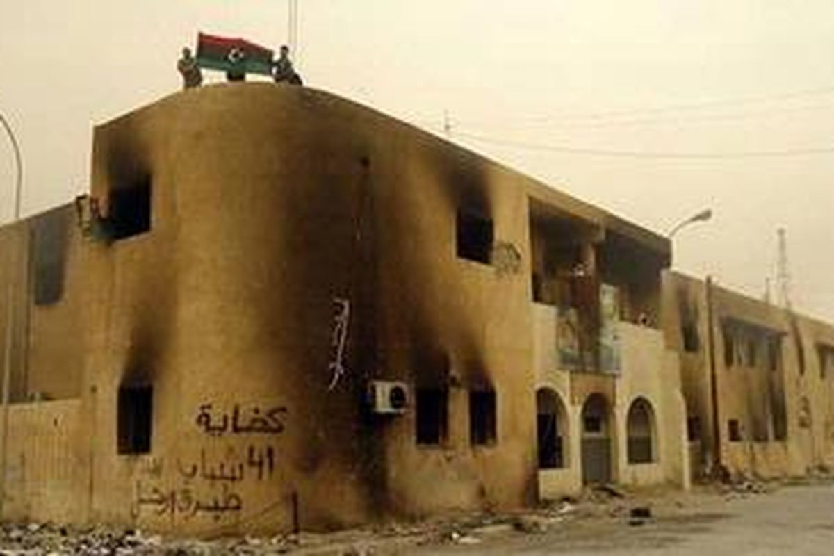 Para pengunjuk rasa Libya, Selasa (22/2/2011), mengibarkan bendera yang dulu digunakan sebelum masa pemerintahan Khadafy di atas sebuah gedung yang hangus terbakar di kota Tobruk, di Libya timur, yang telah jatuh ke tangan para pengunjuk rasa.