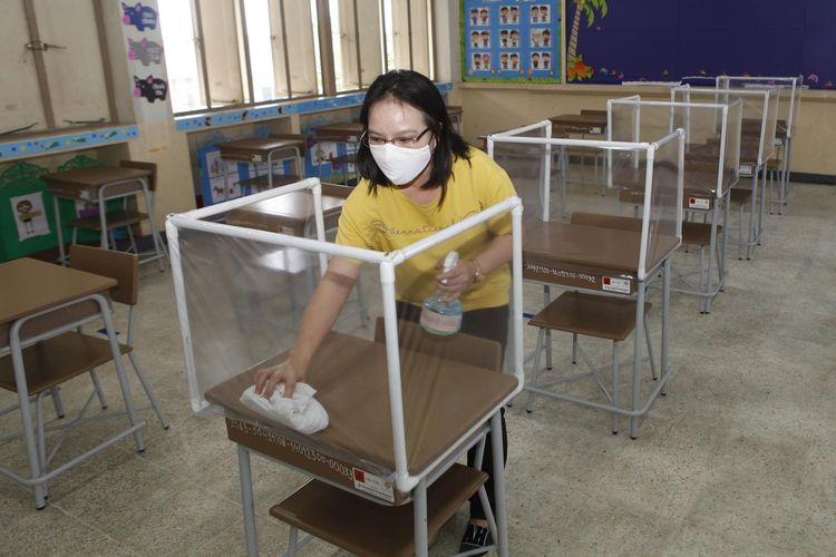 Seorang anggota staf di Or-ngern School di distrik Sai Mai Bangkok membersihkan ruang belajar siswa sebelum sekolah dibuka pada hari Senin. Partisi plastik tembus telah dipasang di atas meja di kafetaria untuk menjaga jarak siswa satu sama lain. 