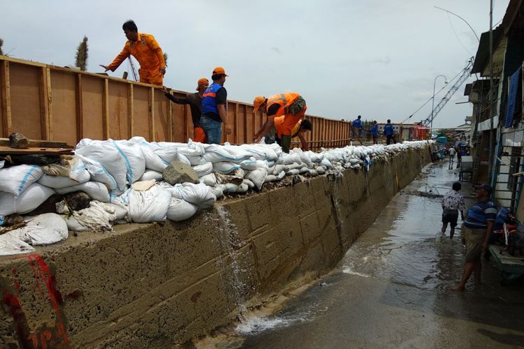 Petugas PPSU dan SDA bahu membahu menutup limpasan air dengan karung pasir di Penjaringan, Jakarta Utara Selasa (5/12/2017)