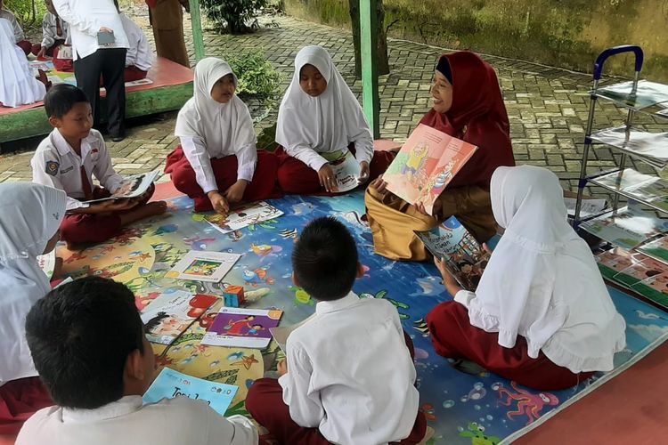 Aktivitas membaca buku bersama antara guru dan murid di SDN 005 Makmur di Kabupaten Pelalawan, Provinsi Riau. 