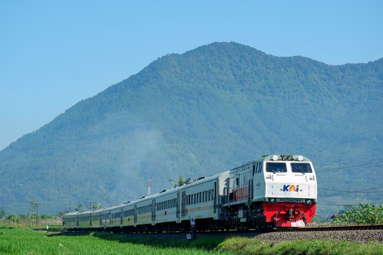 Kereta api dari PT Kereta Api Indonesia (KAI) melintas dengan pemandangan gunung di belakang.