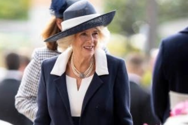 Camilla tampil elegan dengan mengenakan busana berwarna navy, yang terdiri dari gaun panjang midi dengan mantel serasi karya Bruce Oldfield yang menampilkan korset putih dan kerah dua warna. 