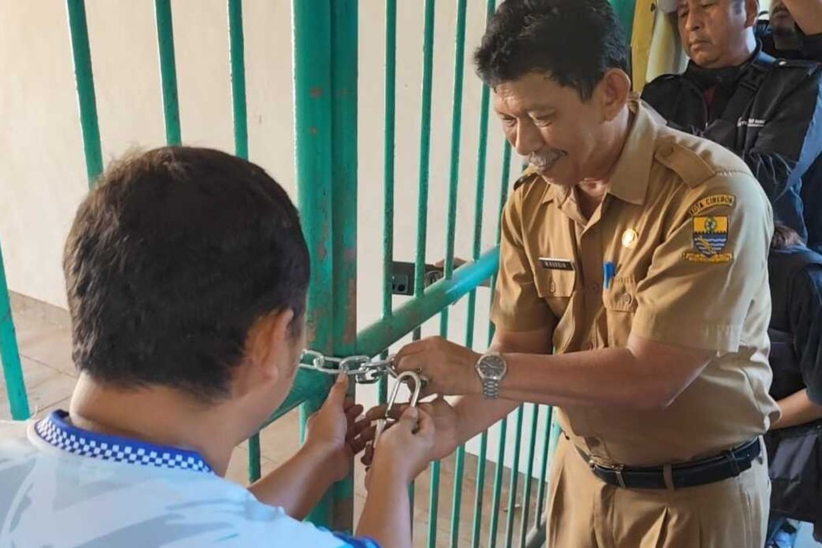 Nurdin (berseragam Dinas) Kepala Bidang Bagian Pengelolaan Barang Milik Daerah Dinas Pengelolaan Keuangan dan Pendapatan Daerah Kota Cirebon menggembok pintu masuk stadion Bima Kota Cirebon pada Senin (28/4/2025) siang.