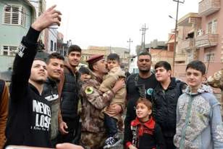 Sejumlah warga kota Mosul berfoto bersama seorang anggota pasukan khusus Irak yang bertempur merebut kota itu dari tangan ISIS.