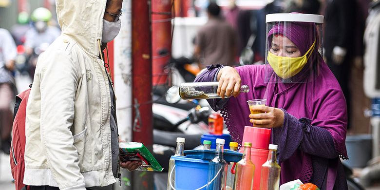 Penjual jamu keliling Tidar (kanan) dengan menggunakan masker dan pelindung wajah melayani pembeli di kawasan Pasar Baru, Jakarta, Selasa (9/6/2020). Tidar menerapkan protokol kesehatan jelang pemberlakuan protokol tatanan normal baru di Jakarta untuk tetap mencari nafkah.