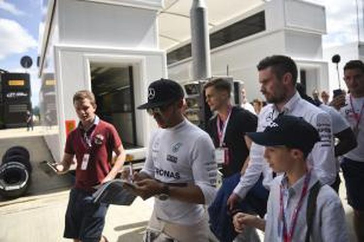 Pebalap Mercedes asal Inggris, Lewis Hamilton, berjalan dikelilingi para fans di paddock Sirkuit Silverstone setelah menyelesaikan sesi kualifikasi GP Inggris, Sabtu (4/7/2015).